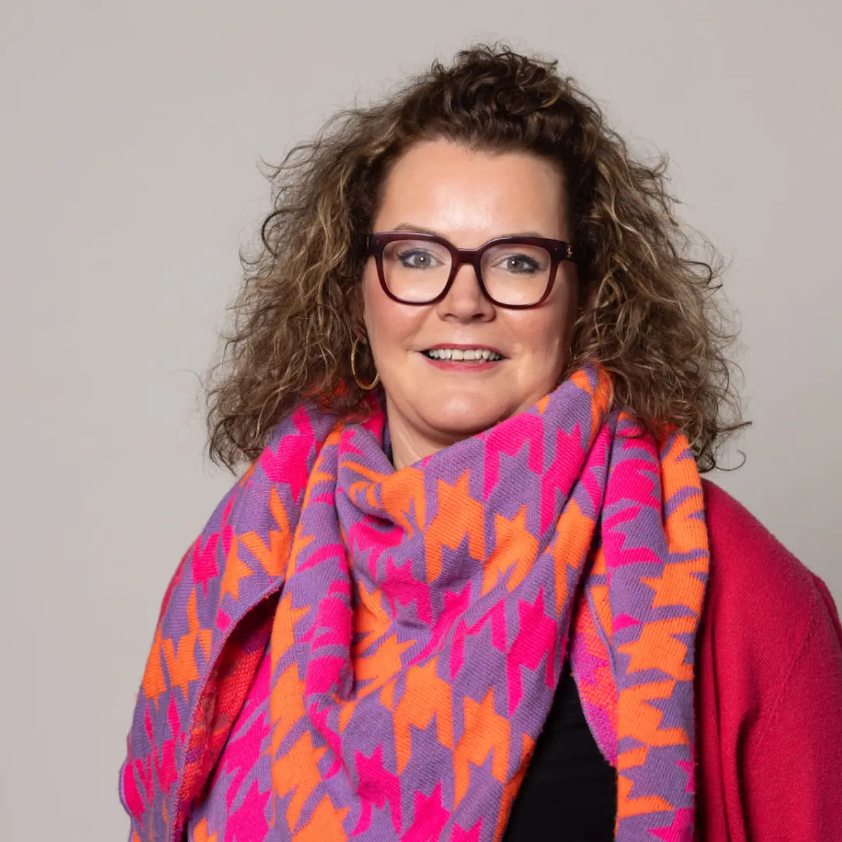 Portrait von Silvia Funke – lächelnd mit Brille, lockigem Haar und buntem Schal vor neutralem Hintergrund